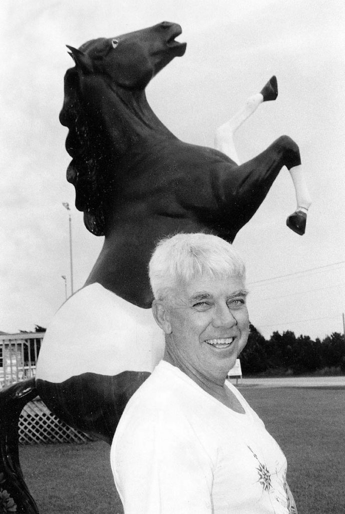Black and white photograph of a man in front of the Pony Island Motel pony statue in Ocracoke, NC